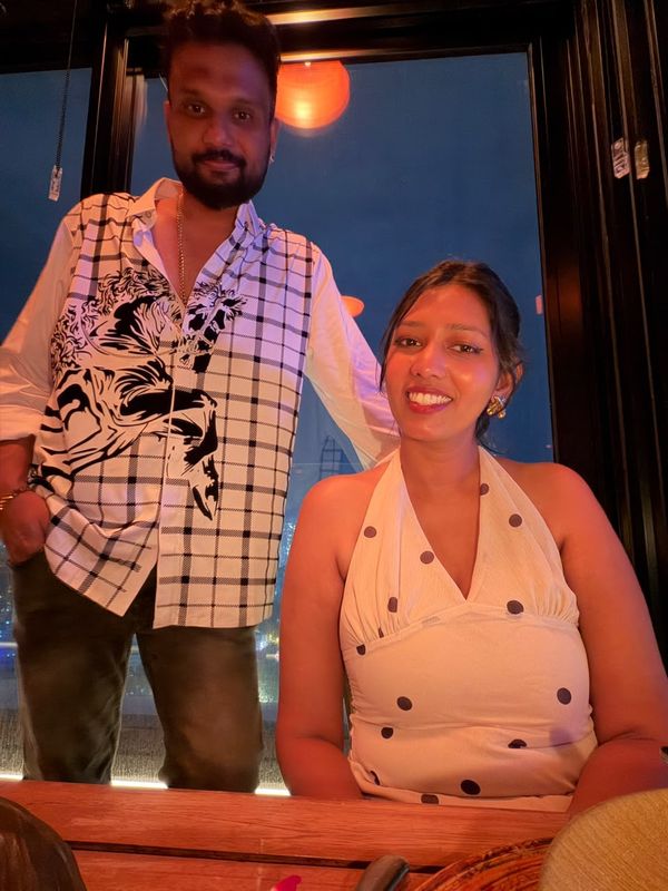 Heshan and Samadei standing together at a rooftop bar with the city lights behind them.